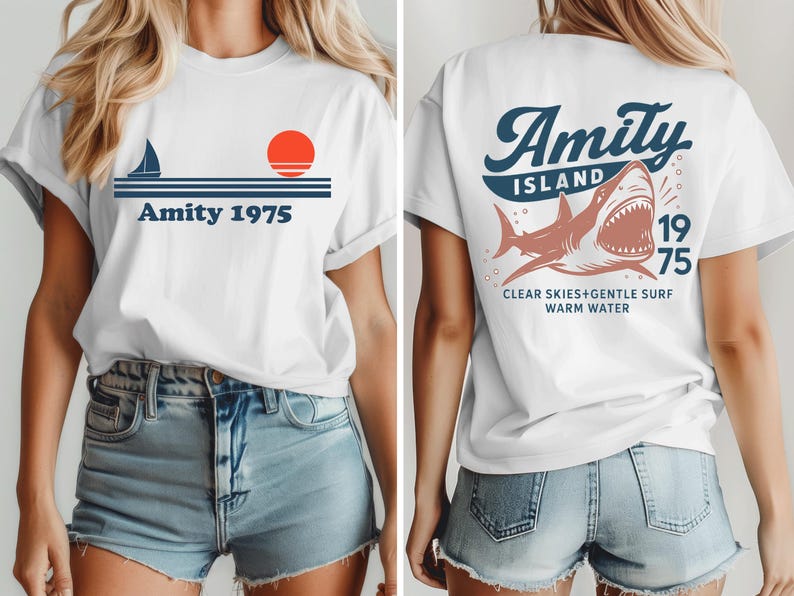 May include: White t-shirt with a nautical design featuring a sailboat, sun, and the text "Amity 1975" on the front. The back of the shirt displays a shark graphic with the words "Amity Island 1975" and "Clear Skies+Gentle Surf Warm Water."