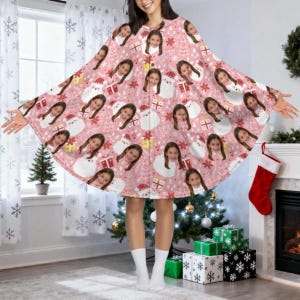 May include: A pink Christmas poncho featuring a repeating pattern of a young girl's face, Santa Claus, snowflakes, and wrapped gifts. The poncho is worn by a person in a room decorated for the holidays.