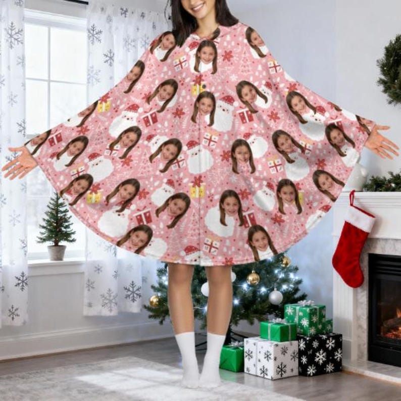 May include: A pink Christmas poncho featuring a repeating pattern of a young girl's face, Santa Claus, snowflakes, and wrapped gifts. The poncho is worn by a person in a room decorated for the holidays.