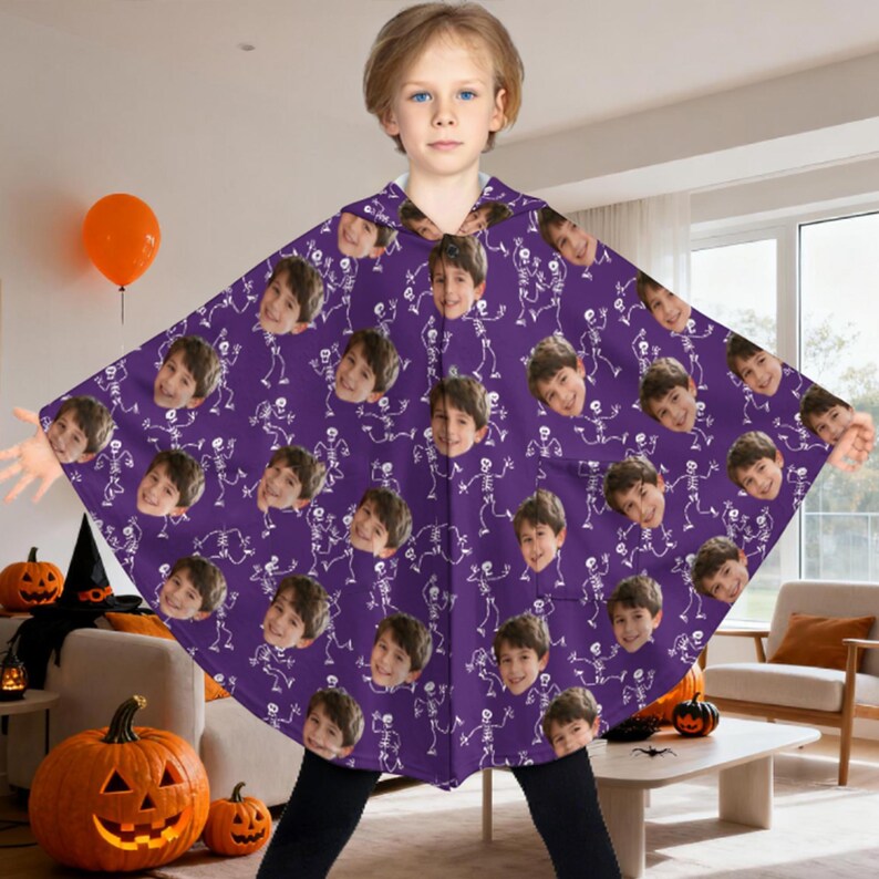 May include: A purple Halloween cape featuring a repeating pattern of white skeletons and a child's face. The cape has a hood and is worn by a child. Pumpkins and an orange balloon are in the background.
