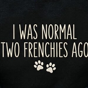 K&ouml;nnte beinhalten: Schwarzer Stoff mit dem wei&szlig;en Text "I WAS NORMAL TWO FRENCHIES AGO" und zwei wei&szlig;en Pfotenabdr&uuml;cken. Der Text ist in einer serifenlosen Schriftart gehalten. Die Pfotenabdr&uuml;cke befinden sich unter dem Text.