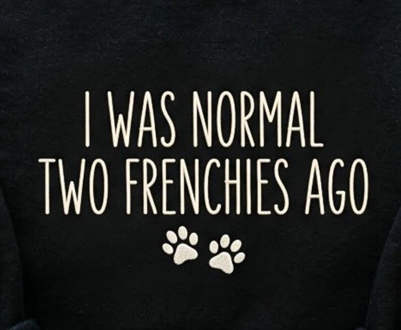 K&ouml;nnte beinhalten: Schwarzer Stoff mit dem wei&szlig;en Text "I WAS NORMAL TWO FRENCHIES AGO" und zwei wei&szlig;en Pfotenabdr&uuml;cken. Der Text ist in einer serifenlosen Schriftart gehalten. Die Pfotenabdr&uuml;cke befinden sich unter dem Text.