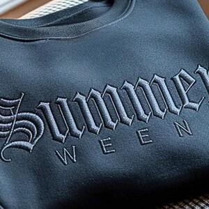 May include: A dark blue sweatshirt with the word "Summer" embroidered in a gothic font across the chest. Below the word "Summer" is the word "WEEN". The sweatshirt has a crew neck.
