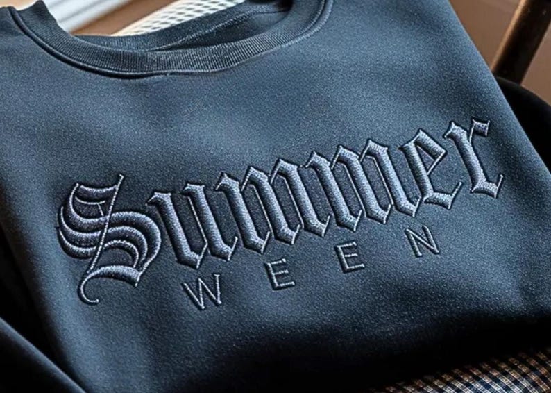 May include: A dark blue sweatshirt with the word "Summer" embroidered in a gothic font across the chest. Below the word "Summer" is the word "WEEN". The sweatshirt has a crew neck.