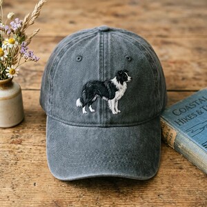 Puede incluir: Una gorra de béisbol gris carbón con un bordado de un perro Border Collie en blanco y negro de perfil. La gorra presenta una corona estructurada, una visera curva y seis paneles con ojales a juego, mostrando un diseño canino detallado.