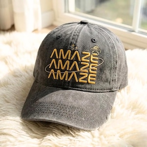 以下が含まれることがあります： 「AMAZE」の文字が黄色で刺繍されたグレーの野球帽。この文字は3回重ねてあり、惑星と星のデザインが施されています。帽子にはカーブしたつばと、上部にボタンが付いています。