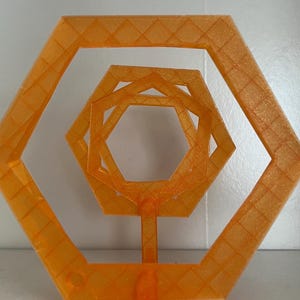 May include: An orange geometric sculpture featuring nested hexagonal shapes. The sculpture is 3D printed and has a textured surface. It stands on a rectangular base and is suitable for home decor or artistic display.