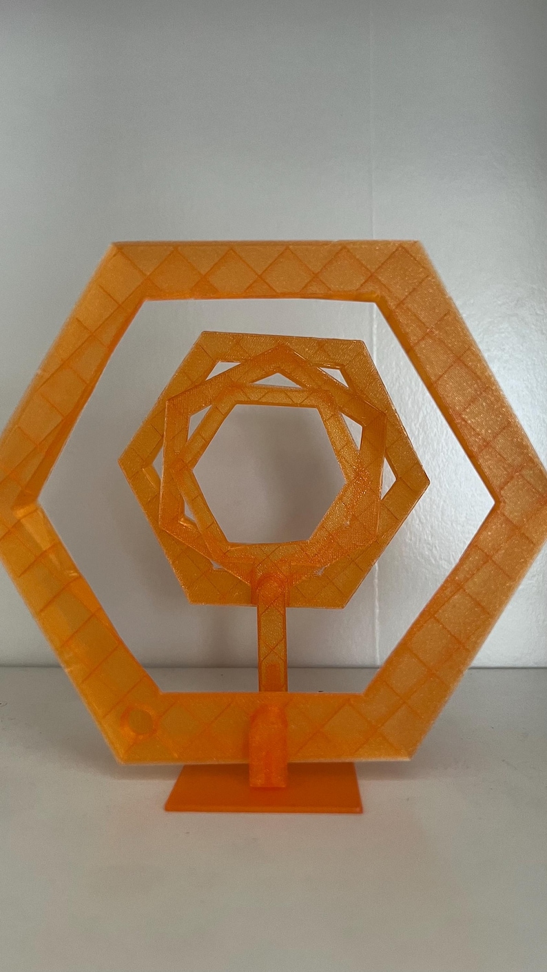 May include: An orange geometric sculpture featuring nested hexagonal shapes. The sculpture is 3D printed and has a textured surface. It stands on a rectangular base and is suitable for home decor or artistic display.