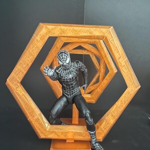 May include: A black and white Spider-Man action figure in a dynamic pose, set against a geometric, orange-colored, hexagonal structure. The figure is detailed with web patterns and stands on a small base.