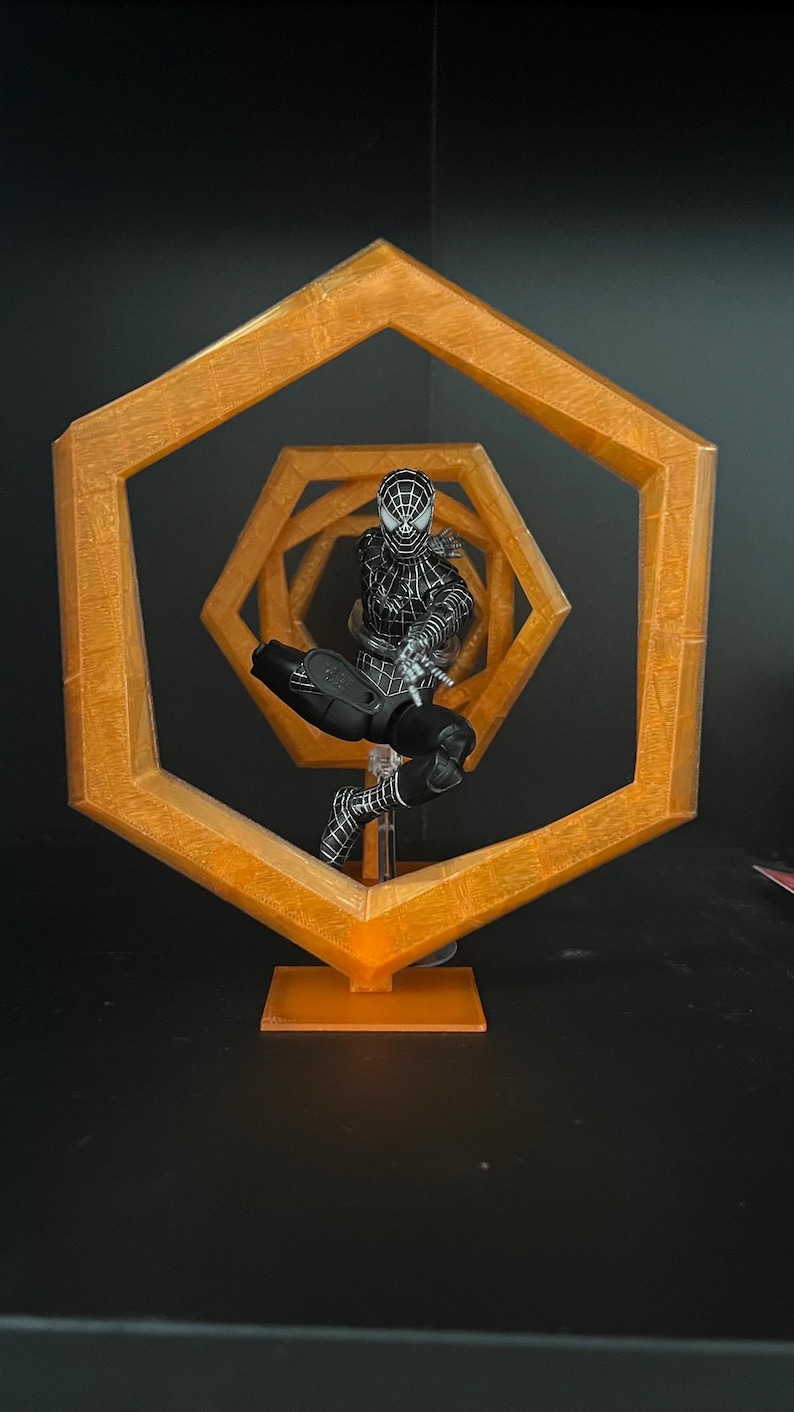 May include: A black and white Spider-Man action figure is positioned within a series of orange hexagonal frames. The figure is in a dynamic pose, with the frames creating a sense of depth and movement. The overall theme is superhero collectibles.