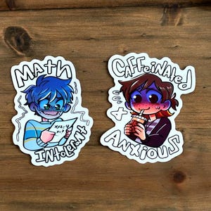 Op de afbeelding: Twee cartoonstickers op een houten oppervlak. Eén sticker toont een blauwharig personage met een papier met de tekst "Math Inherent". De andere sticker toont een personage met een drankje en de tekst "Caffeinated & Anxious".