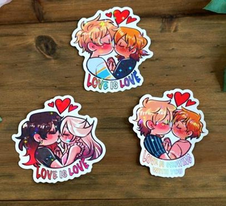 May include: Three stickers depicting cartoon couples kissing, adorned with red heart motifs. The stickers bear the text "LOVE IS LOVE" and "LOVE IS GROWING WITH YOU". The couples have diverse hair colours and wear varied attire. The stickers are presented on a wooden surface.