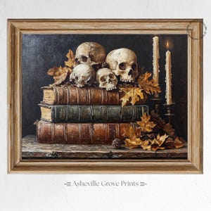 Op de afbeelding: Een ingelijst schilderij met schedels op oude boeken, met herfstbladeren en brandende kaarsen. Het kunstwerk heeft een gotisch thema, tegen een donkere achtergrond. De tekst "Asheville Grove Prints" staat onderaan het frame.