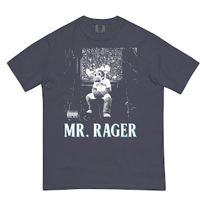 May include: Dark blue t-shirt featuring a graphic of a moose mascot wearing a baseball uniform, seated in a stadium setting. The text "MR. RAGER" is displayed below the image in a teal and white font. The shirt also includes the text "SEATTLE MARINERS 2000-2023".