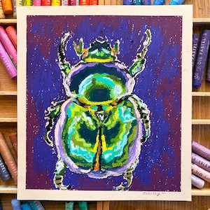 Op de afbeelding: Een origineel olieverfschilderij van een kever, met tinten groen, geel en paars op een vierkant canvas. Het kunstwerk is gesigneerd en omgeven door kleurrijke oliekrijtjes in houten bakken.