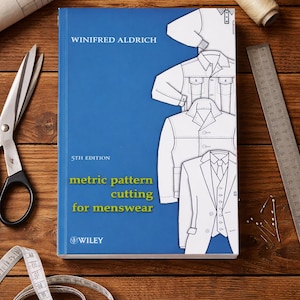 Puede incluir: Un libro azul titulado "Metric Pattern Cutting for Menswear" de Winifred Aldrich, 5ª edición, con ilustraciones de ropa de hombre. Herramientas de costura, incluyendo tijeras, cinta métrica y carretes de hilo, están dispuestas sobre una superficie de madera.