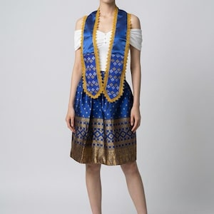 May include: A woman in a blue and gold patterned skirt and sash, paired with a white top. The skirt and sash have detailed gold patterns. She wears gold high heels.