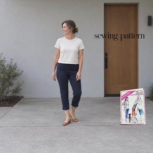 May include: A sewing pattern envelope labeled Stretch & Sew 1644 featuring illustrations of pants and a shirt, displayed alongside a cream short-sleeve t-shirt, dark navy cropped pants, and tan flats. The text sewing pattern is visible.