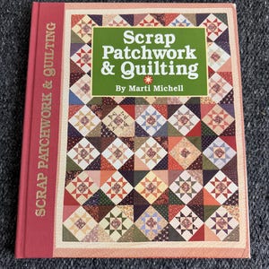 May include: A hardcover book titled "Scrap Patchwork & Quilting" by Marti Michell. The book cover features a patchwork quilt design in various colors, including red, green, and brown. The spine of the book is red with the words "Scrap Patchwork & Quilting" printed vertically.