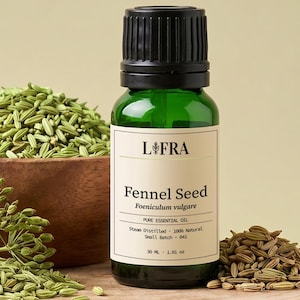 Può includere: Una bottiglia in vetro verde di olio essenziale di semi di finocchio L-FRA con tappo nero e un'etichetta con testo. La bottiglia poggia su una fetta di legno accanto a una ciotola di legno riempita di semi di finocchio e rametti verdi.