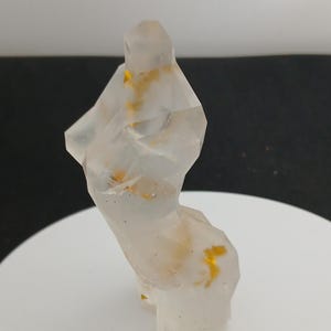 Puede incluir: Una escultura abstracta translúcida de una forma humana. La figura está facetada con un diseño geométrico y contiene inclusiones de color dorado. La escultura se exhibe sobre una superficie blanca contra un fondo oscuro.