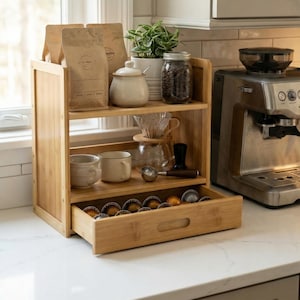 Coffee bar organizer beside an espresso machine with pull-out drawer open showing capsule storage.