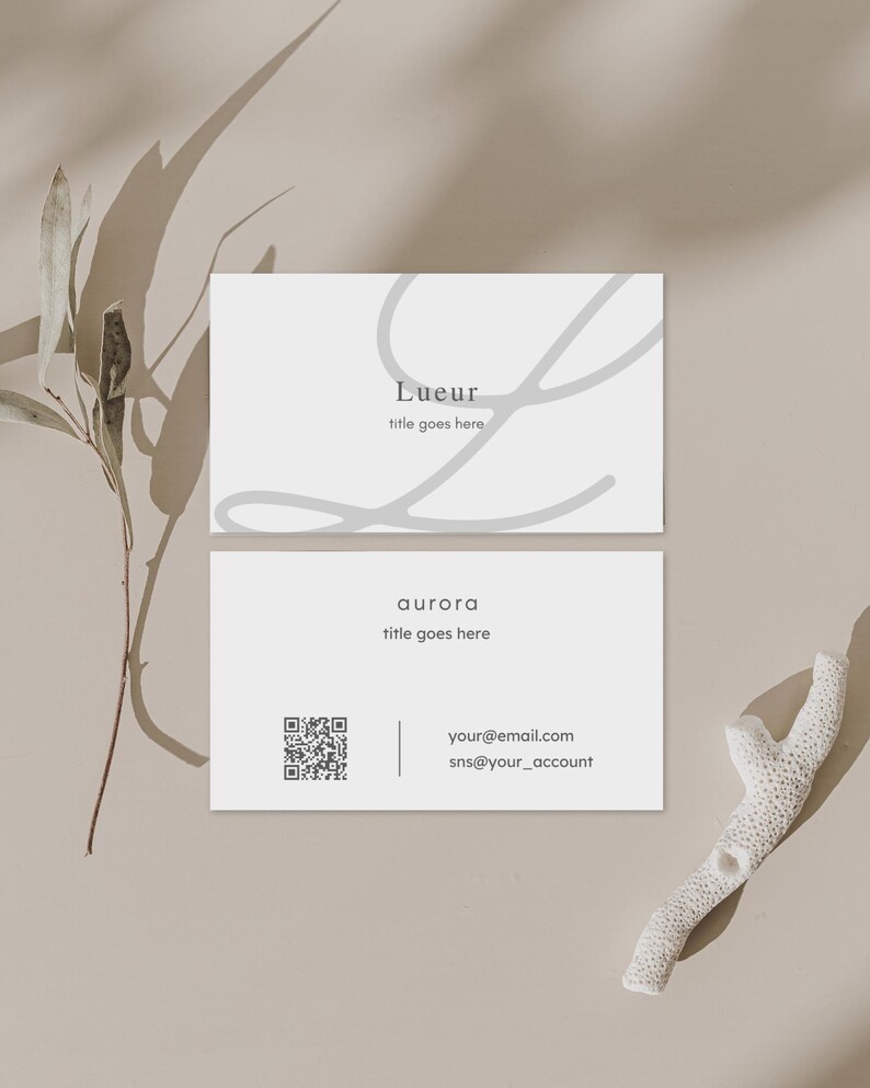 Puede incluir: Dos tarjetas de visita blancas con texto gris y un dise&ntilde;o decorativo gris. La tarjeta superior dice "Lueur" y "title goes here". La tarjeta inferior dice "aurora", "title goes here" e incluye un c&oacute;digo QR e informaci&oacute;n de contacto.