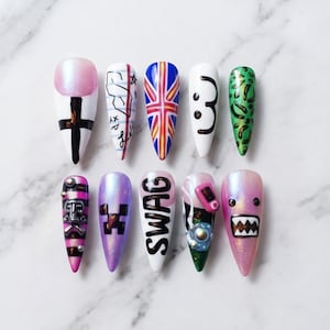 Könnte beinhalten: Ein Set aus zehn mandelförmigen Press-on-Nägeln mit verschiedenen Designs, darunter eine rosa schimmernde French-Spitze mit schwarzem Kreuz, eine britische Flagge, ein grünes Leopardenmuster, das Wort SWAG und diverse grafische Motive.