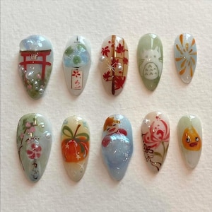 May include: A set of ten almond-shaped nail art designs. Each nail features a unique Japanese-themed illustration, including a red torii gate, a bubble tea design, autumn leaves, a cat, fireworks, and other cultural motifs.