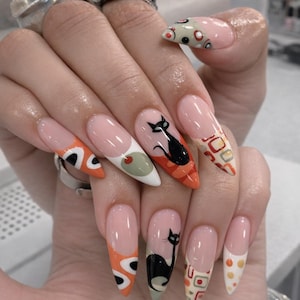 May include: Almond-shaped nails featuring a nude base with intricate nail art designs including black cat silhouettes, olive green circles, orange abstract shapes, and geometric patterns in red, white, and grey tones across the ten fingernails.