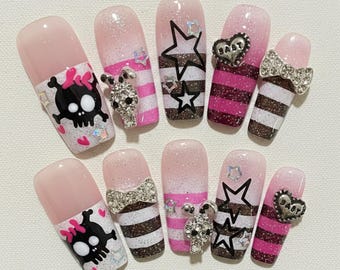 May include: A set of ten artificial nails with a variety of designs. Some nails feature a pink and white ombre effect, while others have black and white stripes, star and skull designs, and rhinestone embellishments.