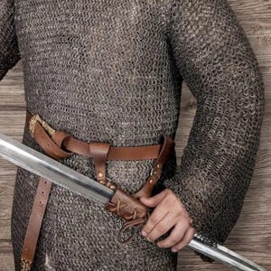 May include: A medieval chainmail shirt with a brown leather belt and a sword in a leather sheath. The chainmail is made of small, interlocking metal rings. The sword has a silver blade.