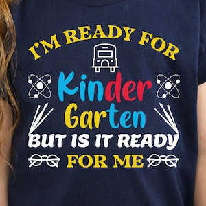 Peut inclure: T-shirt bleu marine avec l'inscription "I'M READY FOR Kindergarten BUT IS IT READY FOR ME" en jaune, bleu et blanc. Le t-shirt présente des graphiques sur le thème de l'école et des sciences. Le t-shirt est porté par une personne aux longs cheveux blonds.