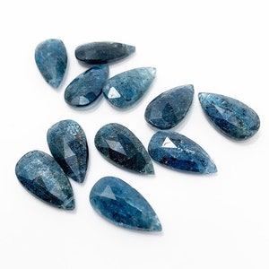 May include: A collection of ten faceted teardrop-shaped blue apatite gemstones. The stones are all approximately the same size and shape, and they have a deep blue color with a slight green tint.