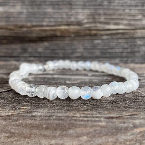 May include: A white moonstone beaded bracelet with a silver clasp. The bracelet is on a wooden surface.