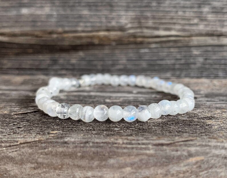 May include: A white moonstone beaded bracelet with a silver clasp. The bracelet is on a wooden surface.