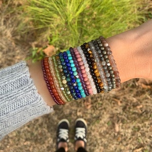 May include: A stack of colorful beaded bracelets made of various gemstones, including amethyst, turquoise, and tiger's eye.
