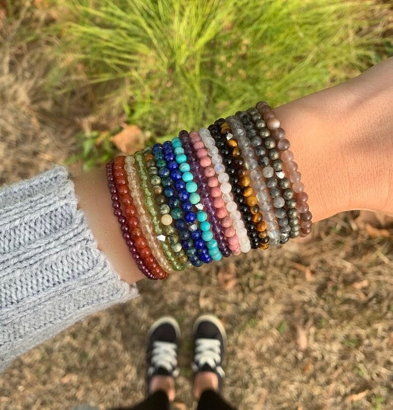 May include: A stack of colorful beaded bracelets made of various gemstones, including amethyst, turquoise, and tiger's eye.