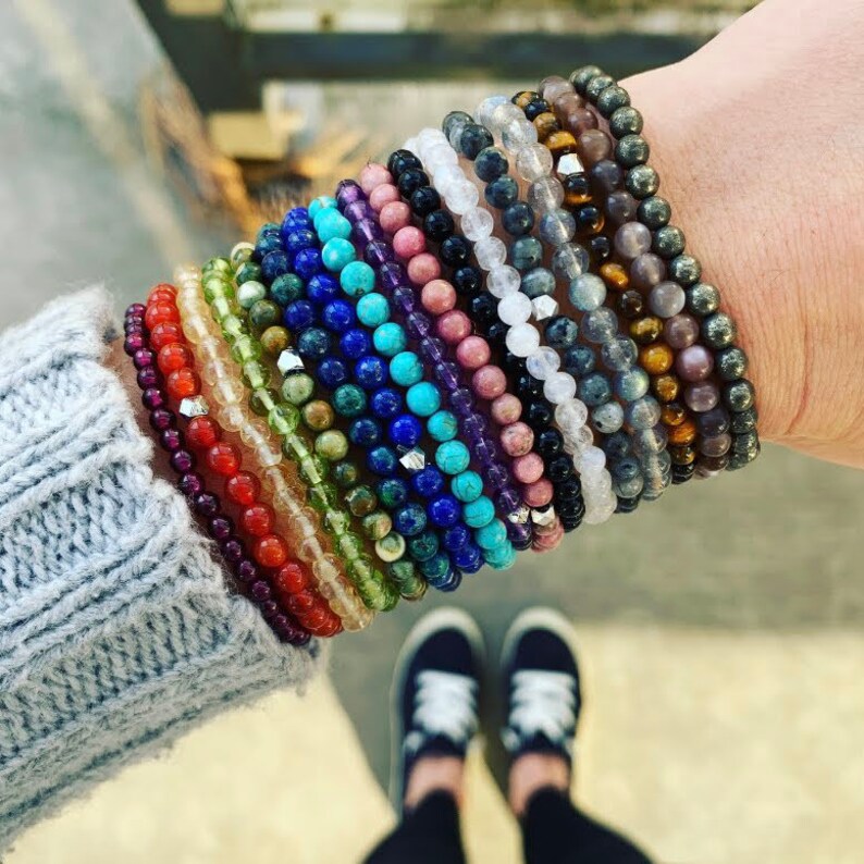 May include: A stack of colorful beaded bracelets made of various gemstones, including turquoise, amethyst, and tiger's eye.