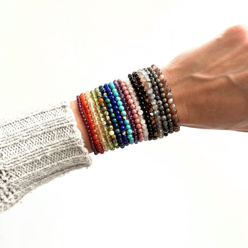 May include: A stack of colorful gemstone bracelets on a person's wrist. The bracelets are made of various stones, including carnelian, amethyst, turquoise, and lapis lazuli.
