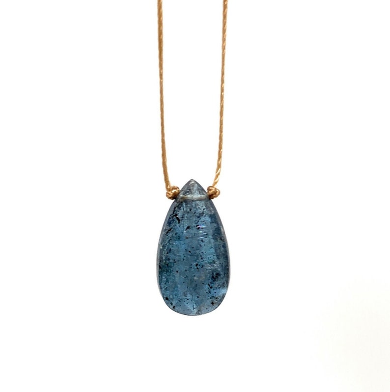 May include: A teardrop-shaped blue gemstone pendant necklace on a thin, light brown cord.