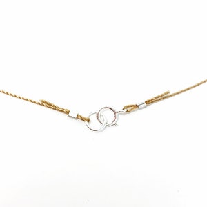 May include: A close-up of a brown cord necklace with a silver clasp. The cord is twisted and has a frayed end.