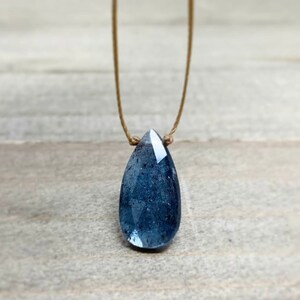 May include: A teardrop-shaped blue gemstone pendant necklace on a brown cord.