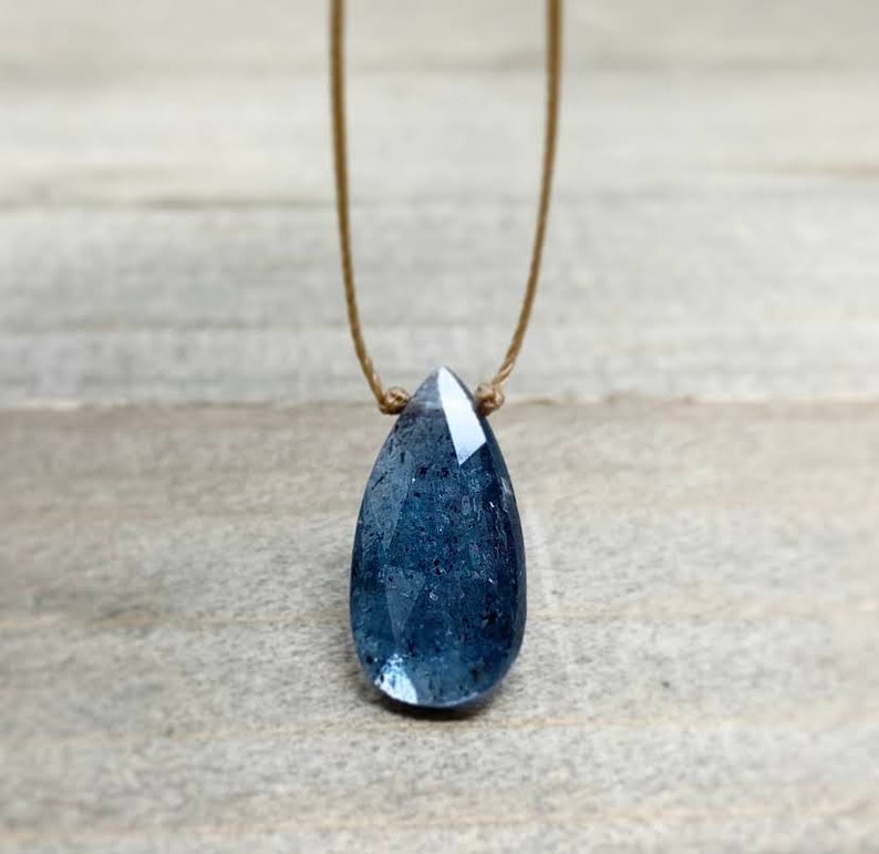 May include: A teardrop-shaped blue gemstone pendant necklace on a brown cord.