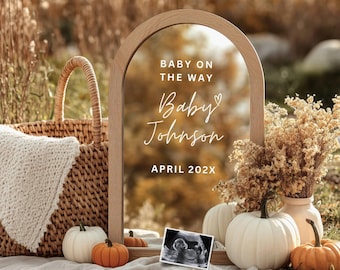 Könnte beinhalten: Eine rustikale Szene im Freien mit einem Holzrahmen-Spiegel, der "Baby on the Way", "Baby Johnson" und "April 202X" ankündigt. Die Szene umfasst einen Weidenkorb, Kürbisse, Trockenblumen und ein Ultraschallbild.