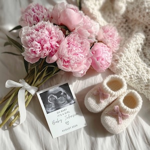 May include: A bouquet of pink peonies with a white ribbon, a sonogram card that reads "OH BABY IT'S A GIRL Baby Johnson August 202X", and two pairs of white knitted baby booties with pink bows.