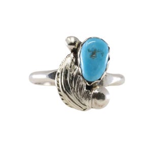 May include: A silver ring featuring a turquoise stone. The ring has a leaf and bead design. The turquoise stone is a bright blue color. The ring is set against a white background.