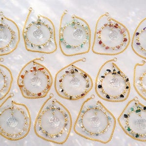 Op de afbeelding: Een verzameling kristallen zonnevangers met goudkleurige frames en kettingen. Elke zonnevanger heeft een centrale facetkristal en een ring van kleurrijke edelstenen. De zonnevangers zijn ontworpen om zonlicht op te vangen en te reflecteren.