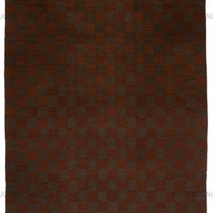 Könnte beinhalten: Ein rechteckiger Teppich mit einem Schachbrettmuster in Braun- und Rotbrauntönen. Das Design des Teppichs zeigt ein sich wiederholendes Raster aus Quadraten, wodurch ein strukturiertes Aussehen entsteht. Die Gesamtästhetik ist warm und einladend.