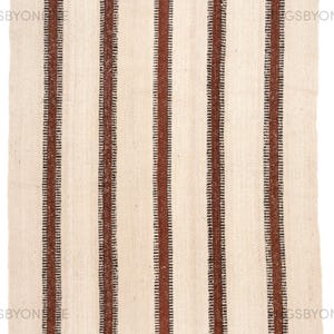 May include: Cream-colored rug with vertical stripes in a dark brown hue. The rug's design features alternating wide and narrow stripes, creating a textured pattern. The rug is made of a woven material.